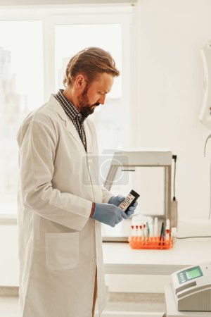 Foto de Hombre vistiendo uniforme científico y máscara está sosteniendo tubos de ensayo en el laboratorio - Imagen libre de derechos