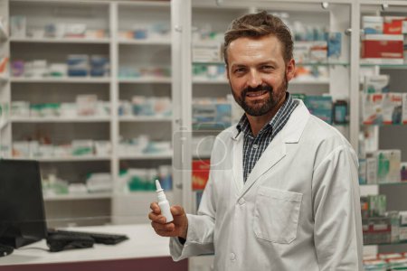 Male pharmacist in white coat holding nose spray while working at a pharmacy. High quality photo