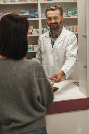 Foto de Hombre farmacéutico en uniforme la venta de medicamentos en la farmacia a una mujer cliente. Foto de alta calidad - Imagen libre de derechos