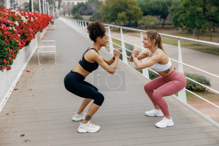 Photo for Two smiling fit women doing workout and squatting together outdoors in the city - Royalty Free Image