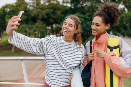 Téléchargez les photos : Deux femmes souriantes de remise en forme faisant selfie au téléphone après la matinée d'entraînement en plein air - en image libre de droit