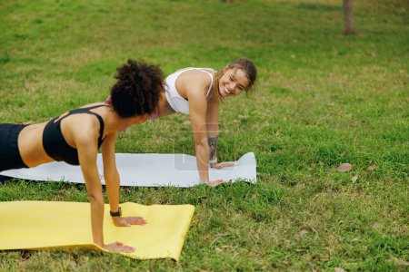 Foto de Las mujeres jóvenes al aire libre en el parque de pie en la pose de tablón haciendo flexiones o ejercicios de flexiones - Imagen libre de derechos