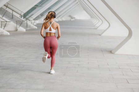 Foto de Mujer joven en ropa deportiva se ejecuta en los edificios modernos de fondo. Concepto de estilo activo - Imagen libre de derechos