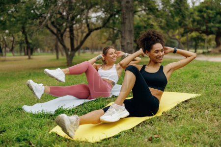 Photo for Young sports women pump the press on yoga mat in natural parkland. Active lifestyle concept - Royalty Free Image