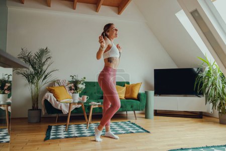 Téléchargez les photos : Une femme danse dans un salon devant un canapé vert, avec une plante d'intérieur dans le coin - en image libre de droit