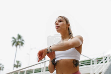 Téléchargez les photos : Jeune femme en forme qui regarde smartwatch et compte les calories brûlées. Concept de vie saine - en image libre de droit