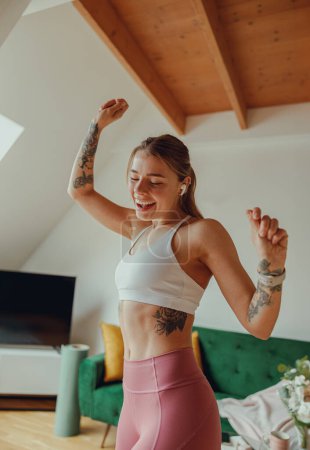 Foto de Mujer sonriente baila a la música en la sala de estar con pisos de madera y plantas de interior - Imagen libre de derechos