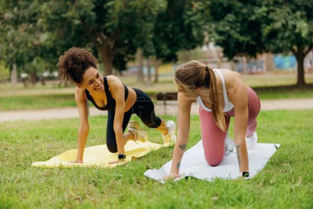 Photo for Two female friends training together while standing in plank pose on fitness mat in natural parkland - Royalty Free Image