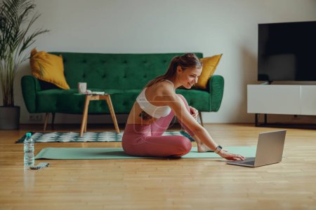 Foto de Una mujer está sentada en un piso de madera en ropa deportiva y el uso de ordenador portátil - Imagen libre de derechos