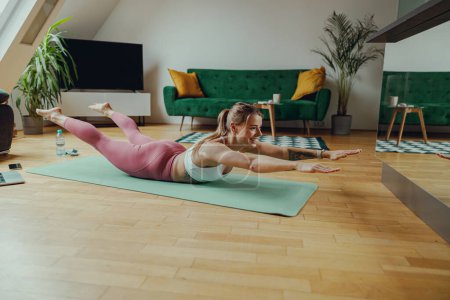 Foto de Una mujer está practicando yoga en un suelo de madera en su sala de estar. Concepto de entrenamiento en casa - Imagen libre de derechos