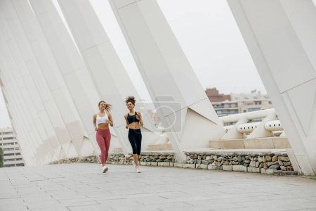 Foto de Dos mujeres jóvenes en ropa deportiva se ejecutan en los edificios modernos de fondo. Concepto de estilo activo - Imagen libre de derechos