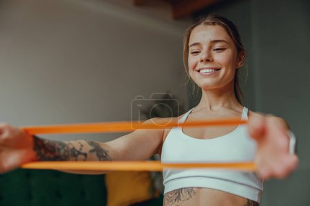 Photo for The woman is smiling as she grips a resistance band, targeting muscles in her waist to tone up - Royalty Free Image