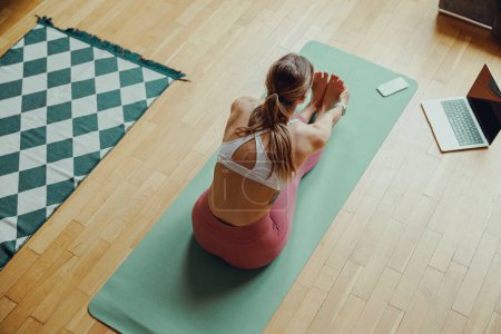 Téléchargez les photos : Une femme est assise sur un tapis de yoga en bois dur dans un salon, profitant du temps libre - en image libre de droit