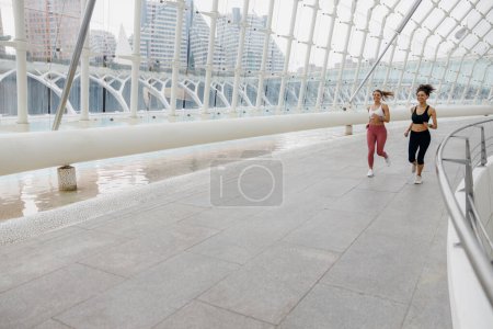 Photo for Two young women in sportswear are running on modern buildings background. Active lifestyle concept - Royalty Free Image