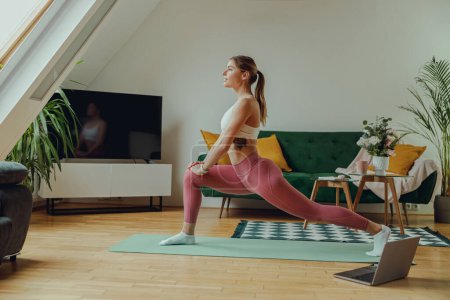 Téléchargez les photos : Une femme pratique une posture de yoga sur un tapis de yoga en bois dans sa maison - en image libre de droit