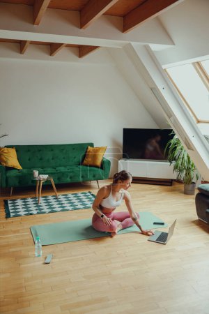 Téléchargez les photos : Une femme est confortablement assise sur un tapis de yoga dans une chambre avec parquet - en image libre de droit