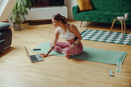Foto de Mujer en esterilla de yoga en ropa deportiva, utilizando portátil en pisos de madera - Imagen libre de derechos
