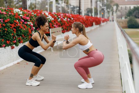 Photo for Two smiling fit women doing workout and squatting together outdoors. Active lifestyle concept - Royalty Free Image