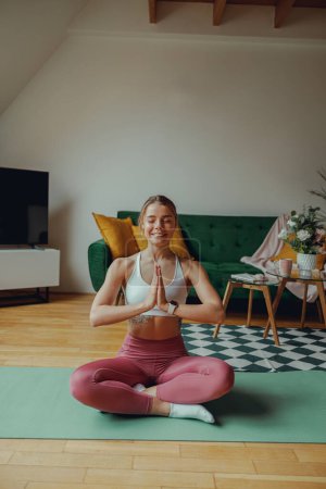 Téléchargez les photos : Une femme est tranquillement assise sur un tapis de yoga dans un salon rempli de parquet - en image libre de droit