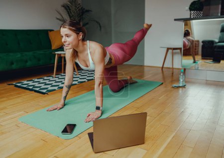 Téléchargez les photos : Femme pratique le yoga sur un tapis devant un ordinateur portable, en se concentrant sur les articulations, les jambes, les cuisses et les genoux - en image libre de droit
