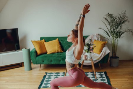 Foto de Una mujer está practicando yoga en una sala de estar con pisos de madera y un sofá verde - Imagen libre de derechos