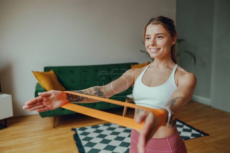 Photo for A woman is exercising with a resistance band in a living room. Home workout concept - Royalty Free Image