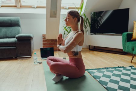 Téléchargez les photos : Une femme est assise sur un tapis de yoga dans le salon par des plantes de la maison et design d'intérieur élégant - en image libre de droit