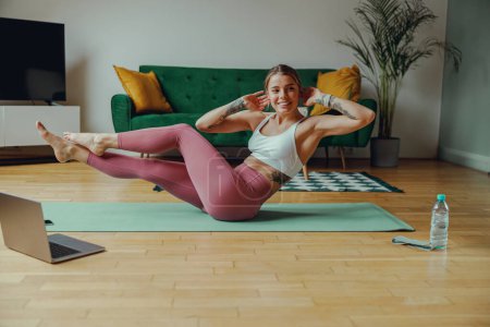 Photo for The woman in sportswear doing exercises on a yoga mat in a living room with hardwood flooring - Royalty Free Image