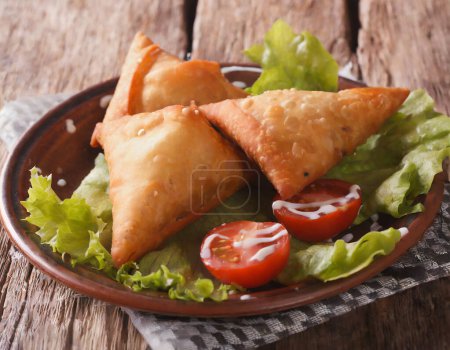 Photo for Delicious Indian samosa pastry presented on a plate with tomatoes and lettuce on a wooden table. - Royalty Free Image
