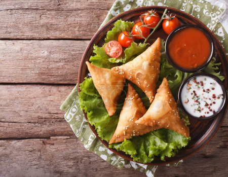 Photo for Delicious Indian samosa pastry presented on a plate with tomatoes and lettuce on a wooden table. - Royalty Free Image