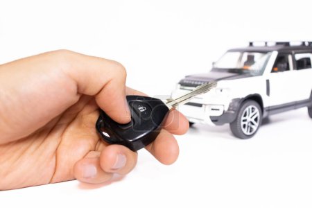 Car key in hand with car on the background isolated on white. Car stuff concept. After some edits.