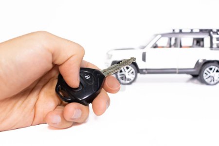 Car key in hand with car on the background isolated on white. Car stuff concept. After some edits.