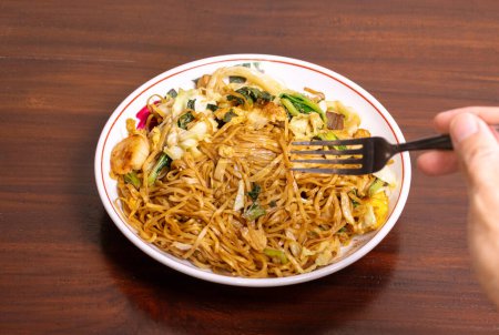 Fried noodle with chicken and vegetables in a white bowl on a wooden table. After edits.