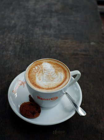Photo for Caffe Latte. Cup of coffee with a sweet cookie. capucino kopi dari Resto Banaran 9 kopi di Semarang. nampak disajikan dengan wadah cangkir berwarna putih , lambar putih, ditambahkan biskuit coklat dan biji kopi, juga disiapkan sendok untuk mengaduk. - Royalty Free Image