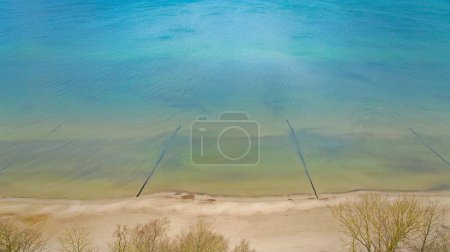 Téléchargez les photos : Un tir de drone capture la plage de Gaski dans la voïvodie de Poméranie occidentale, en Pologne. L'image montre les eaux bleu-vert de la mer Baltique, une vaste plage de sable et des arbres sans feuilles sur les dunes. Prise en février hiver. - en image libre de droit