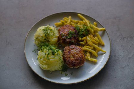 Classic Polish cuisine: pork mince burgers, mashed potatoes, yellow wax beans, breadcrumb-topped, garnished with finely chopped dill. 