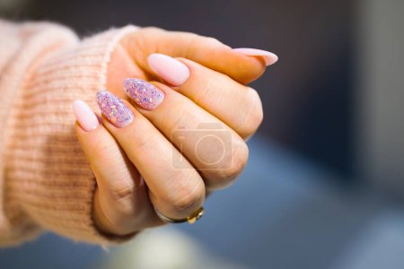 Photo for A meticulously maintained woman's hand featuring stunning pink gel nails. The nails are perfectly painted, with two adorned with stylish, multicolored glitter. Well-groomed and nourished. - Royalty Free Image