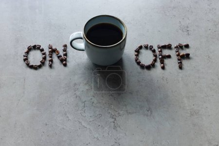 La photo montre "on" et "off" avec des grains de café, avec une tasse de café noir fraîchement infusé placé entre eux. Il sert de métaphore pour allumer l'esprit, le corps et l'individu pour stimuler l'action.