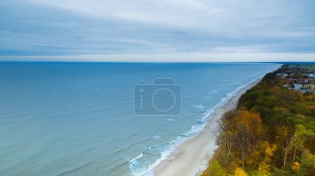 Drohnenaufnahme des Gaski Leuchtturms, Polen, an einem bewölkten Novembertag. Das ruhige Meer, sanfte Wellen und ein leerer Strand schaffen eine ruhige Küstenlandschaft, die einen friedlichen Rückzugsort an der Ostsee bietet. 