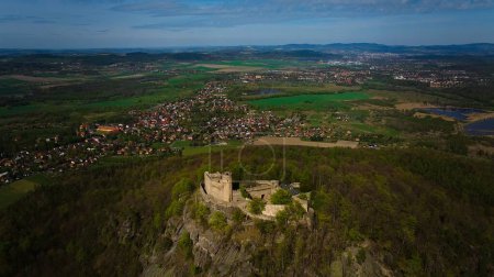 An aerial view captures the medieval Chojnik Castle atop a mountain in the Karkonosze range. The ancient fortress stands proudly amidst the scenic landscape, blending history with nature.