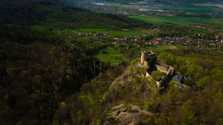 Une vue aérienne capture le château médiéval de Chojnik au sommet d'une montagne dans la chaîne de Karkonosze. L'ancienne forteresse se dresse fièrement au milieu du paysage pittoresque, mêlant histoire et nature.