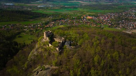 An aerial view captures the medieval Chojnik Castle atop a mountain in the Karkonosze range. The ancient fortress stands proudly amidst the scenic landscape, blending history with nature.