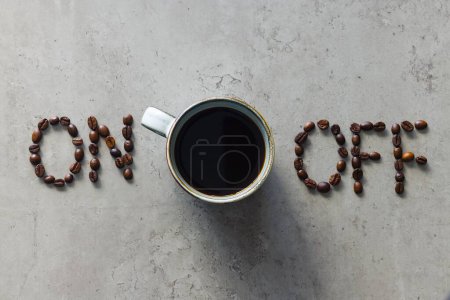 Das Foto zeigt "ein" und "aus" buchstabiert mit Kaffeebohnen, zwischen denen eine Tasse frisch gebrühten schwarzen Kaffee platziert ist. Es dient als Metapher für die Entzündung von Geist, Körper und Individuum, um zum Handeln anzuregen.
