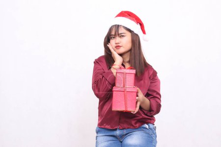 Photo for Beautiful young graceful southeast asian girl carrying gift box at christmas wearing santa claus hat modern red shirt outfit holding cheeks white background for promotion and advertising - Royalty Free Image