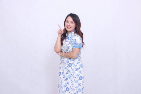 Photo for Beautiful smile asian woman wearing modern chinese dress arms crossed pointing right up isolated on white background. happy Chinese New Year - Royalty Free Image