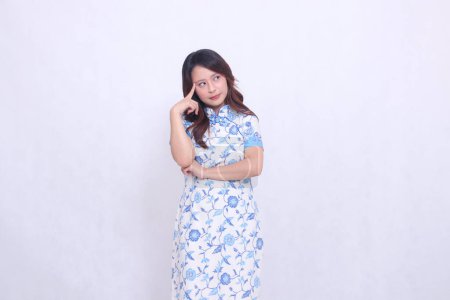 Beautiful Chinese Javanese woman with a flat smile wearing a modern Chinese dress, arms crossed, thinking on a white background. happy Chinese New Year