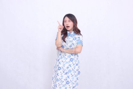 Photo for Beautiful surprised Javanese Chinese woman wearing a modern Chinese dress with her hands pointing at the top on a white background. happy Chinese New Year - Royalty Free Image