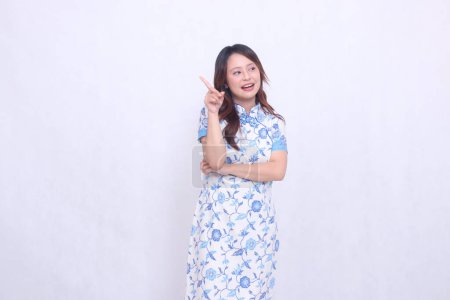Beautiful Chinese Javanese woman smiling to the left wearing a modern Chinese dress, pointing her hand crookedly to the right on a white background. happy Chinese New Year