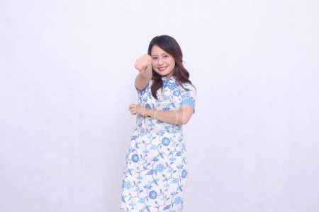 Beautiful cheerful Javanese Chinese woman wearing a modern Chinese dress with her arms crossed pointing at the camera on a white background. happy Chinese New Year