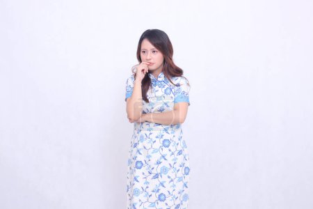 beautiful Javanese Chinese woman thinking wearing a modern Chinese dress with her arms crossed, left side view on a white background. happy Chinese New Year